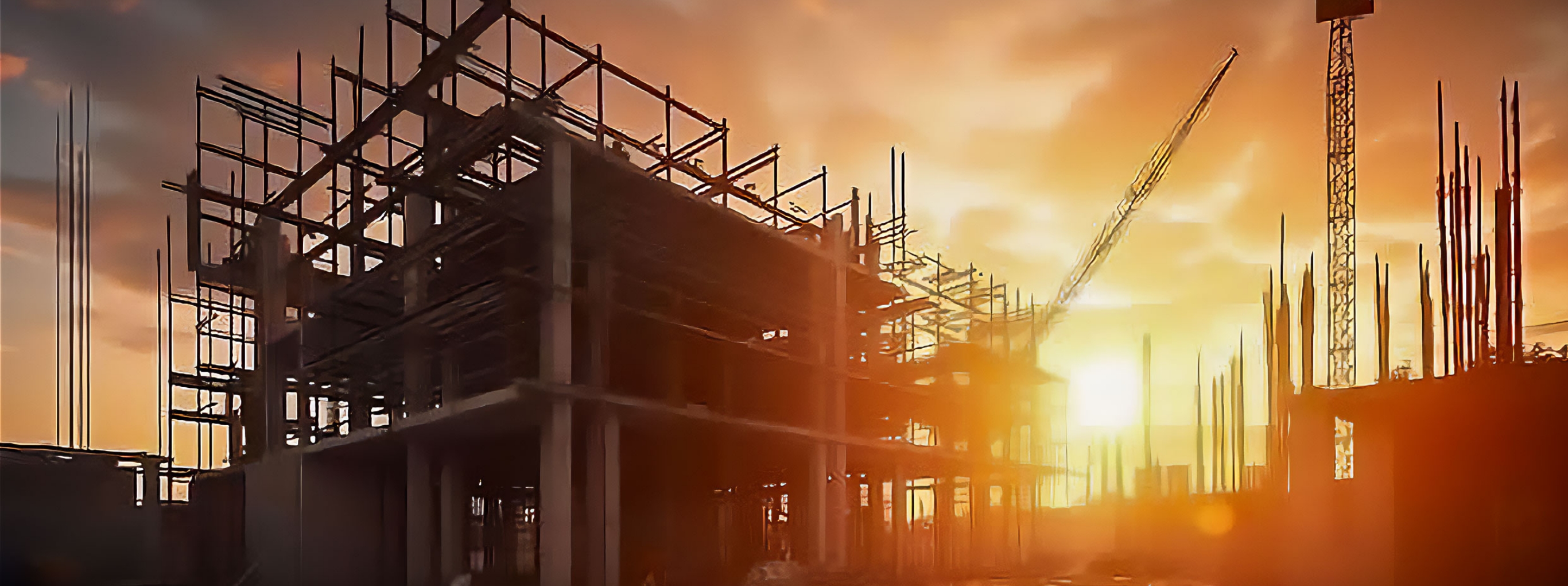 夕日を背景に、建設中の建物の鉄骨構造とクレーンが影のように浮かび上がっている工事現場の風景。