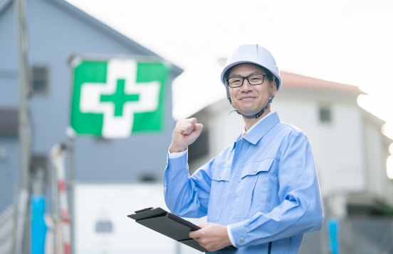 経営理念「品質向上」のイメージ。ヘルメットを着用した作業員が安全旗の前でガッツポーズを取っている。